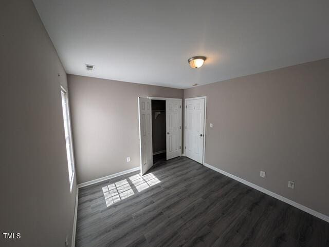 unfurnished bedroom with dark wood finished floors, visible vents, a closet, and baseboards