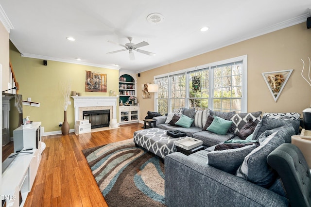 living room with hardwood / wood-style flooring, ornamental molding, built in features, and ceiling fan