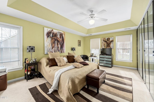 bedroom featuring multiple windows, light colored carpet, and a raised ceiling