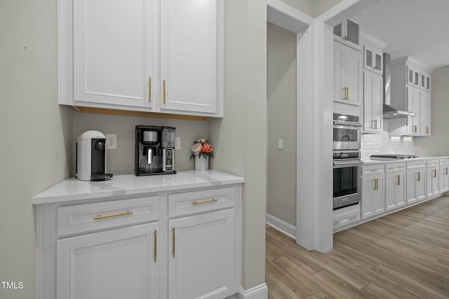 kitchen featuring white cabinetry, stainless steel appliances, light wood-type flooring, and wall chimney range hood