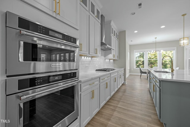 kitchen featuring decorative light fixtures, sink, white cabinets, stainless steel appliances, and wall chimney range hood