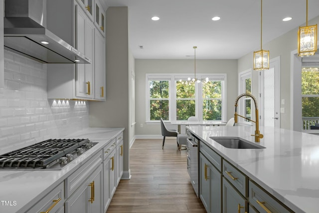 kitchen with pendant lighting, wall chimney exhaust hood, gray cabinets, and sink