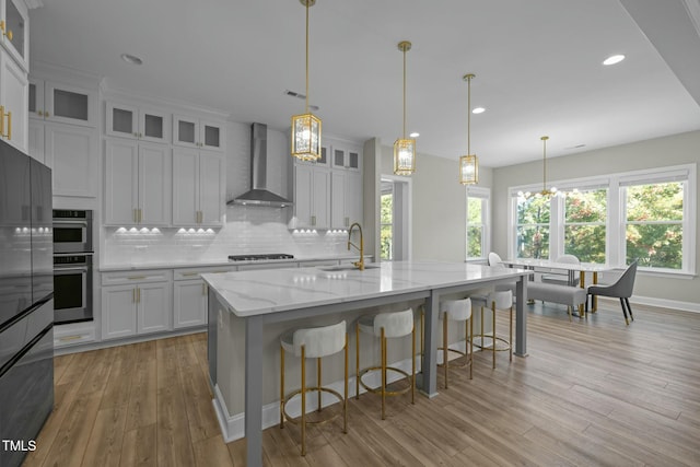 kitchen with white cabinetry, wall chimney exhaust hood, decorative light fixtures, and a large island with sink