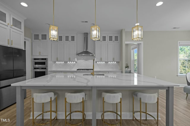 kitchen with appliances with stainless steel finishes, a large island, wall chimney range hood, and light stone counters