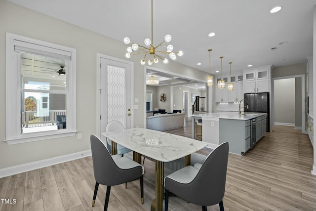 dining space featuring sink, ceiling fan with notable chandelier, and light hardwood / wood-style floors