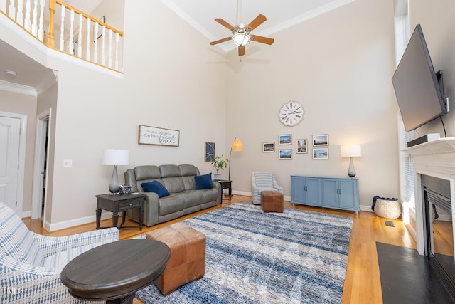 living room with ceiling fan, ornamental molding, a high ceiling, and light wood-type flooring