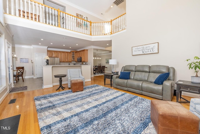 living room with ornamental molding, a high ceiling, and light wood-type flooring