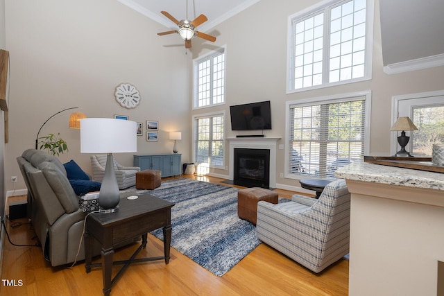 living room featuring ornamental molding, a towering ceiling, ceiling fan, and light hardwood / wood-style flooring