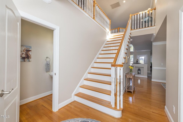 staircase featuring hardwood / wood-style flooring, a towering ceiling, and ornamental molding