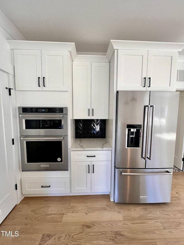 kitchen with appliances with stainless steel finishes, light hardwood / wood-style flooring, tasteful backsplash, and white cabinetry