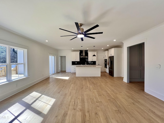 kitchen with a kitchen island with sink, decorative light fixtures, white cabinets, high end black fridge, and wall chimney range hood