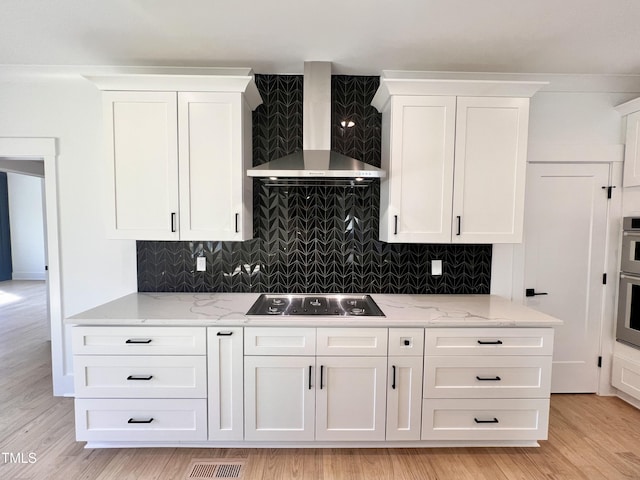 kitchen featuring appliances with stainless steel finishes, white cabinetry, light stone countertops, and wall chimney range hood