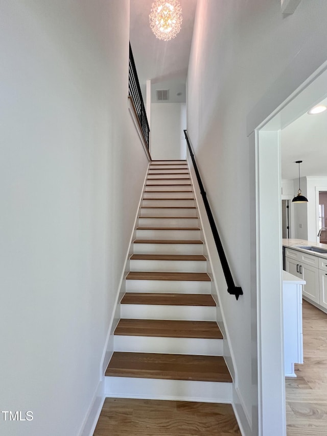 stairway with sink, hardwood / wood-style flooring, and a chandelier