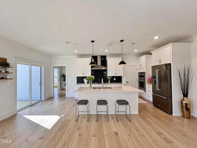 kitchen featuring sink, white cabinetry, stainless steel appliances, wall chimney exhaust hood, and an island with sink