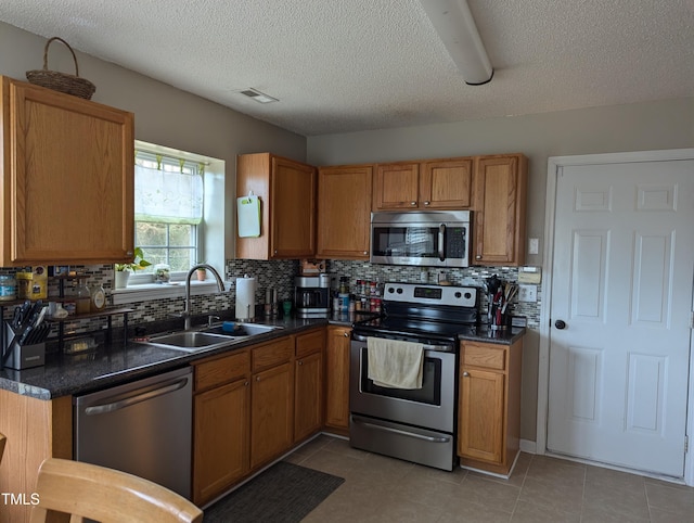 kitchen featuring sink, backsplash, light tile patterned floors, stainless steel appliances, and a textured ceiling