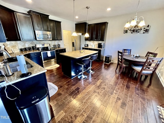 kitchen featuring dark wood-type flooring, stainless steel appliances, light stone countertops, a kitchen island, and decorative light fixtures