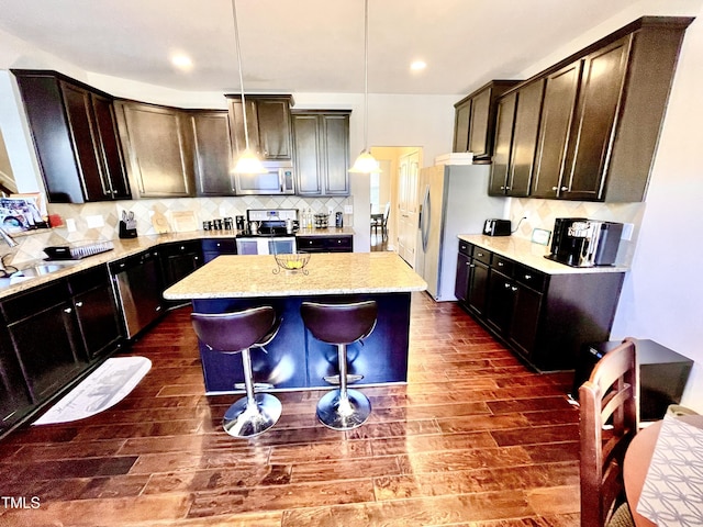 kitchen with a kitchen island, appliances with stainless steel finishes, decorative light fixtures, a breakfast bar area, and dark wood-type flooring