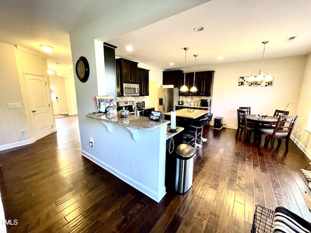 kitchen with a breakfast bar, decorative light fixtures, appliances with stainless steel finishes, kitchen peninsula, and light stone countertops