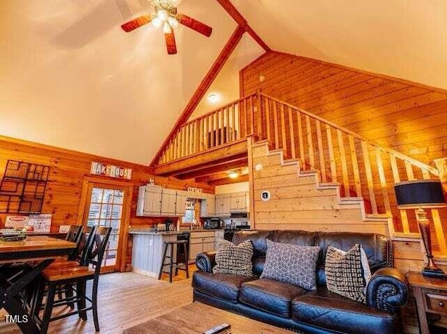 living room with sink, wood walls, high vaulted ceiling, light hardwood / wood-style flooring, and ceiling fan