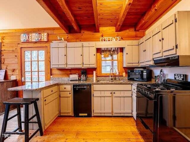 kitchen with sink, a breakfast bar area, beam ceiling, black appliances, and kitchen peninsula