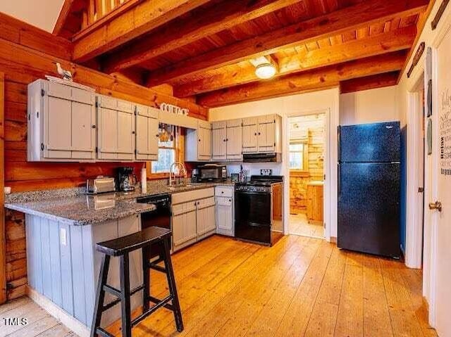 kitchen with sink, light hardwood / wood-style flooring, dark stone countertops, black appliances, and beamed ceiling