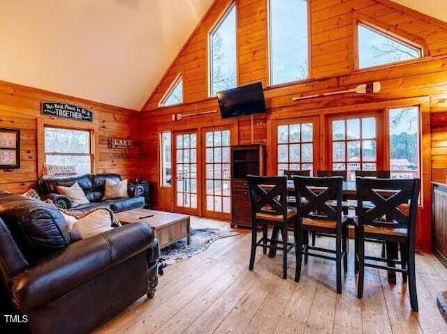 living room with high vaulted ceiling, wooden walls, and light hardwood / wood-style flooring