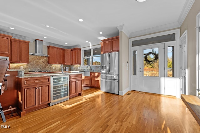 kitchen featuring wine cooler, stainless steel fridge, wall chimney exhaust hood, crown molding, and light hardwood / wood-style flooring