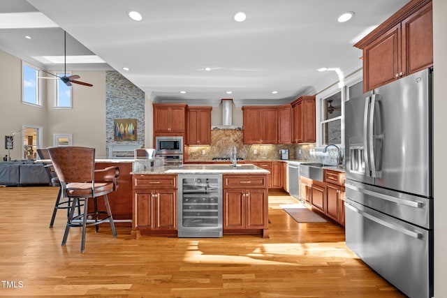 kitchen featuring sink, a breakfast bar area, wine cooler, stainless steel appliances, and wall chimney range hood