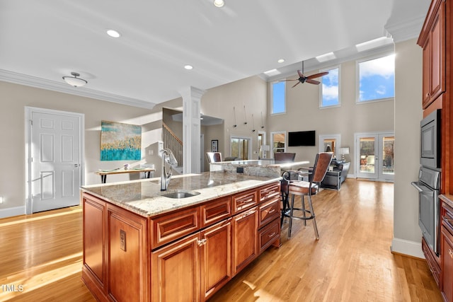 kitchen with sink, appliances with stainless steel finishes, light stone countertops, a center island with sink, and ornate columns