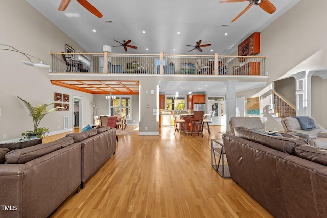 living room featuring ceiling fan with notable chandelier, light wood-type flooring, decorative columns, and a high ceiling