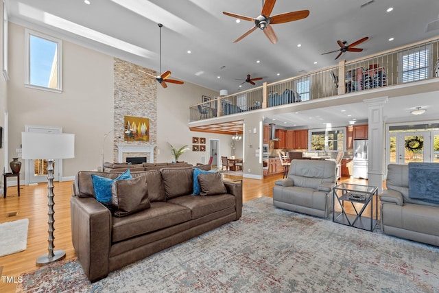 living room with decorative columns, a stone fireplace, a towering ceiling, and light hardwood / wood-style floors