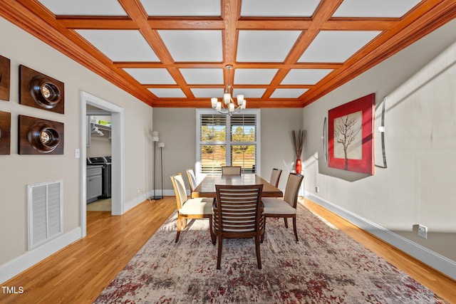 dining area with crown molding, coffered ceiling, a chandelier, and light hardwood / wood-style flooring