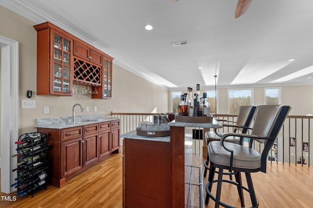 bar featuring light stone counters, sink, ornamental molding, and light wood-type flooring