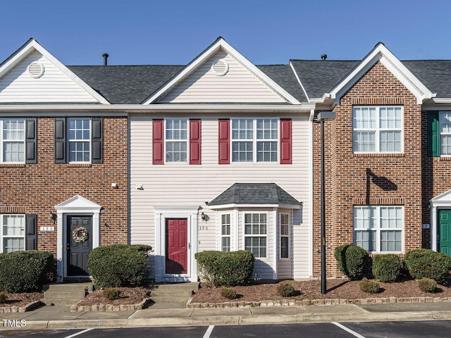 townhome / multi-family property featuring brick siding and roof with shingles