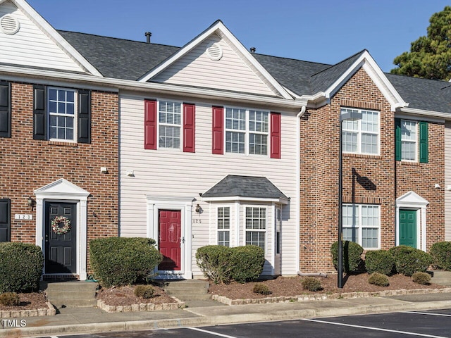 multi unit property with roof with shingles, uncovered parking, and brick siding