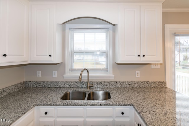 kitchen featuring white cabinetry, crown molding, sink, and light stone counters