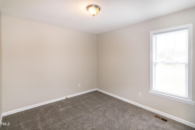 spare room with dark colored carpet, plenty of natural light, and a textured ceiling