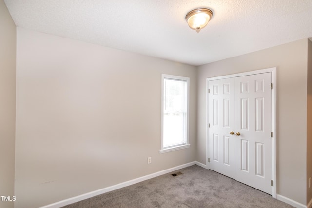 unfurnished bedroom featuring light carpet, a closet, and a textured ceiling