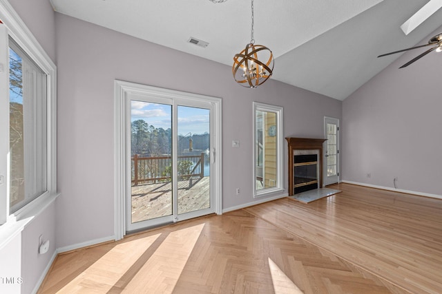 unfurnished living room featuring visible vents, baseboards, a high end fireplace, lofted ceiling with skylight, and ceiling fan with notable chandelier