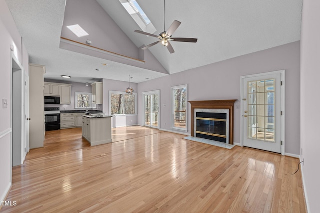 unfurnished living room featuring light wood-type flooring, a skylight, a ceiling fan, and a high end fireplace