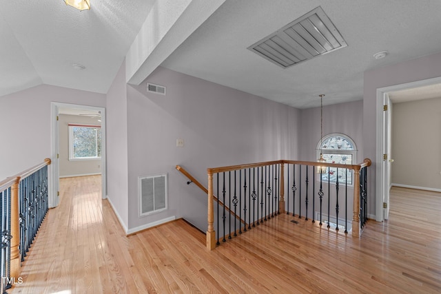 corridor with baseboards, visible vents, wood finished floors, and an upstairs landing