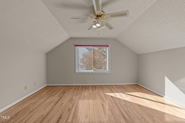 additional living space with baseboards, ceiling fan, wood finished floors, vaulted ceiling, and a textured ceiling