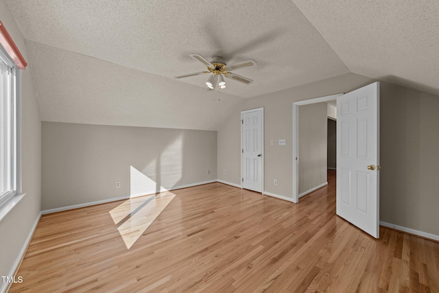 additional living space with a textured ceiling, a ceiling fan, baseboards, vaulted ceiling, and light wood-type flooring