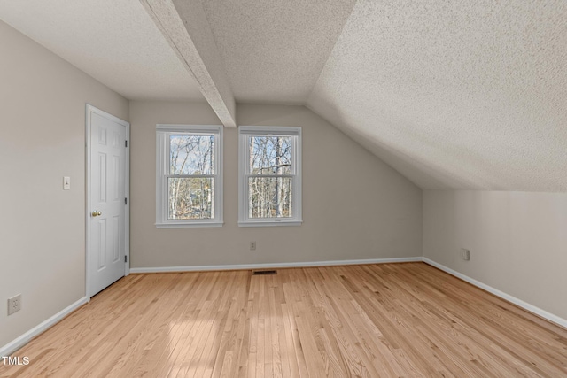 bonus room featuring a textured ceiling, visible vents, baseboards, vaulted ceiling, and light wood-style floors