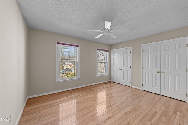 unfurnished bedroom with baseboards, a textured ceiling, wood finished floors, and multiple closets