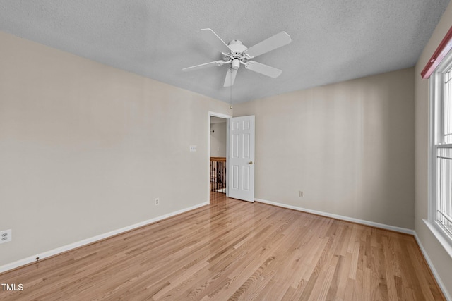 spare room with a ceiling fan, light wood-style flooring, baseboards, and a textured ceiling