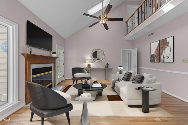 living room with baseboards, a ceiling fan, a premium fireplace, wood finished floors, and high vaulted ceiling