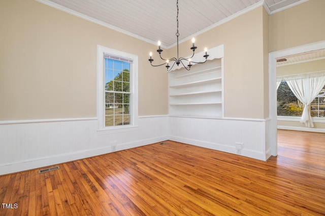 unfurnished dining area featuring ornamental molding, a healthy amount of sunlight, a notable chandelier, and built in shelves