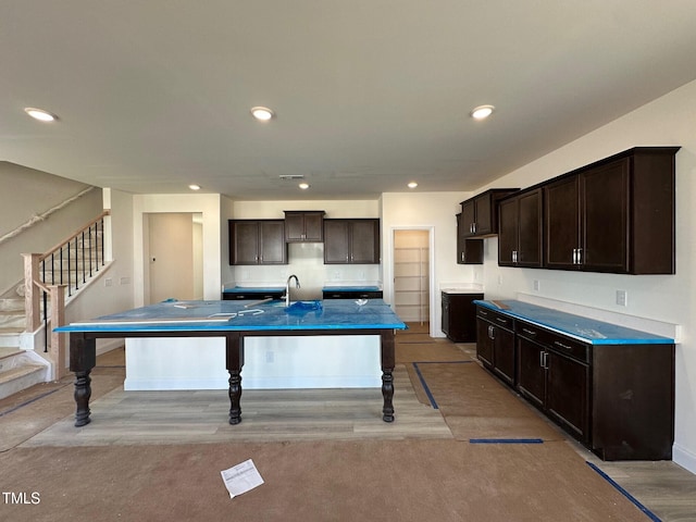 kitchen featuring dark brown cabinets, light wood-style flooring, a center island with sink, and recessed lighting