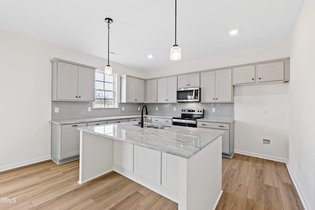 kitchen with sink, hanging light fixtures, a kitchen island with sink, light stone counters, and stainless steel appliances